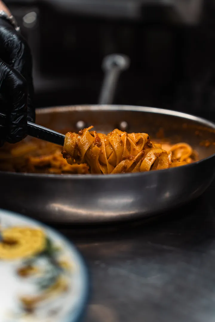 Le pappardelle al ragù d'anatra sollevate con le pinze dalla padella, nella cucina della Locanda degli Scaligeri